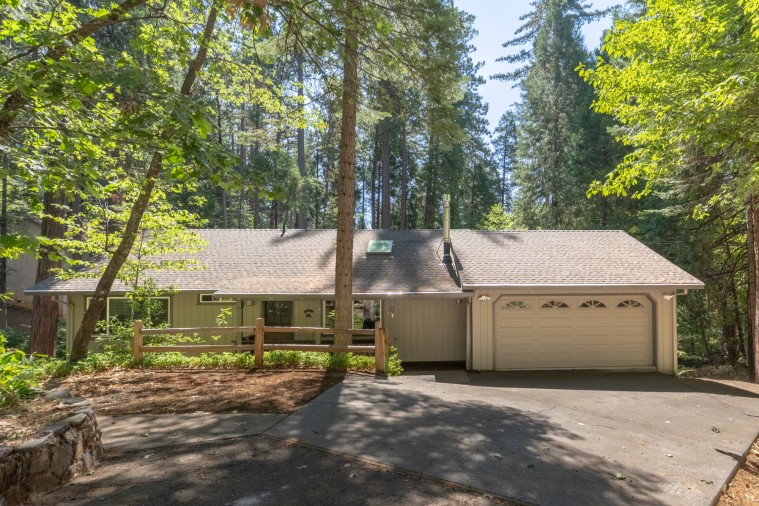 A charming woodland retreat nestled among towering pines, offering a peaceful escape in a serene forest setting with spacious parking and a welcoming front porch.